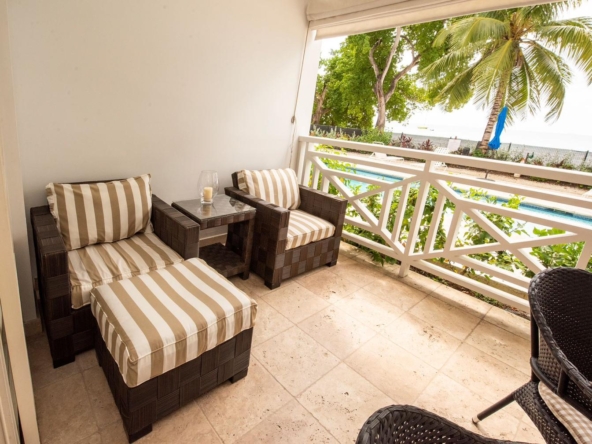 Image of a spacious balcony with comfortable lounge chairs overlooking the turquoise sea, showcasing a beachfront 2 bedroom apartment in Paynes Bay with stunning ocean views and high-end amenities.